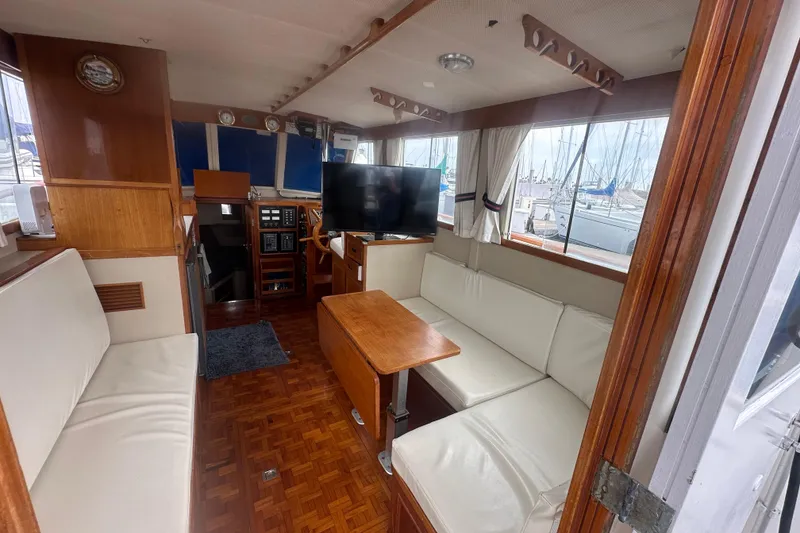 Slide: The Image of 1976 Grand Banks Sedan interior with white seating, wooden accents, and a view of marina. - 5