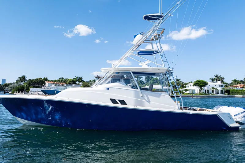 Slide: The Image of 2016 SeaVee 430 boat on water, blue hull, clear sky, waterfront homes in background. - 105