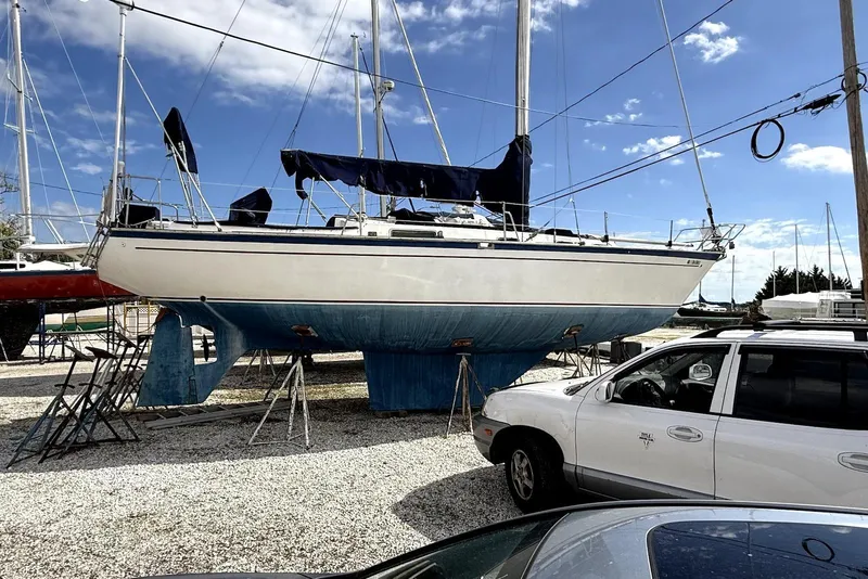 The Image of 1985 Morgan 380 sailboat on stands in a boatyard under a clear blue sky. - 0