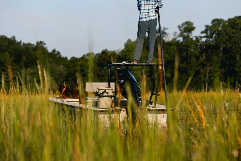 Slide: The Image of Delta Boatworks D18, 2026 model, navigating through lush marshland with a person and dog onboard. - 7