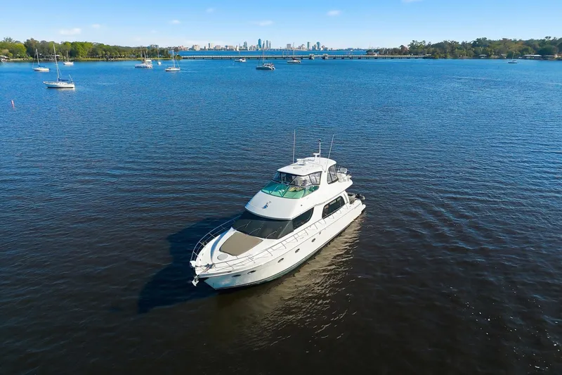Slide: The Image of 2006 Carver 56 Voyager yacht cruising on a serene lake with city skyline backdrop. - 2