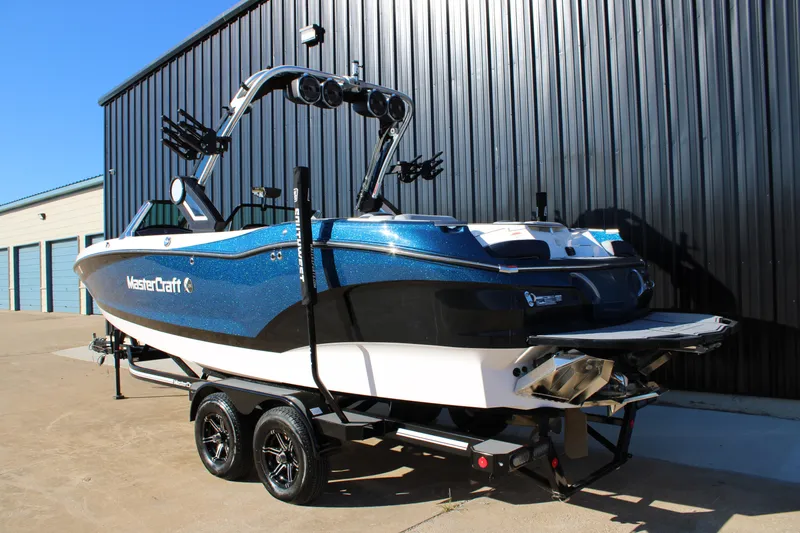 Slide: The Image of 2022 MasterCraft X24 boat on trailer, blue and black design, parked by a building. - 2