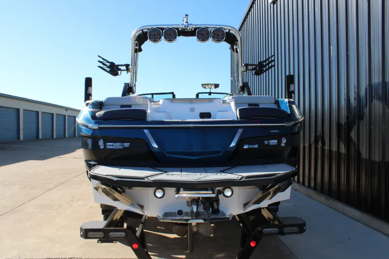 Slide: The Image of 2022 MasterCraft X24 boat, rear view, parked near storage units and metal building. - 3