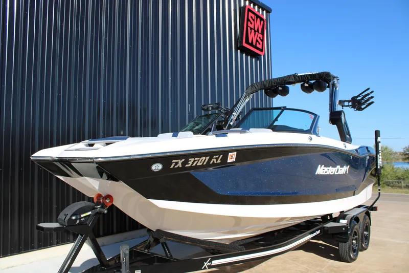 Slide: The Image of 2022 MasterCraft X24 boat on trailer, displayed outdoors with black building backdrop. - 5