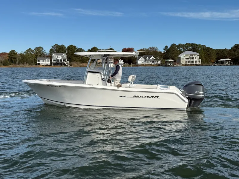 Slide: The Image of 2012 Sea Hunt Triton 240 boat cruising on a calm lake with houses in the background. - 4