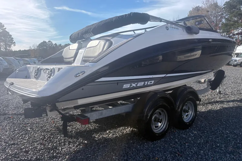 Slide: The Image of 2019 Yamaha Boats SX210 on trailer, parked on gravel under clear sky. - 2