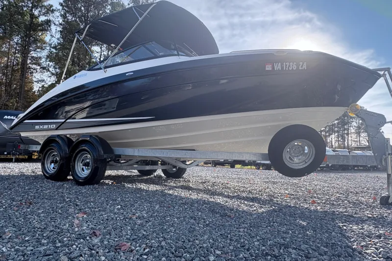 Slide: The Image of 2019 Yamaha Boats SX210 on trailer, parked on gravel with trees in background. - 3