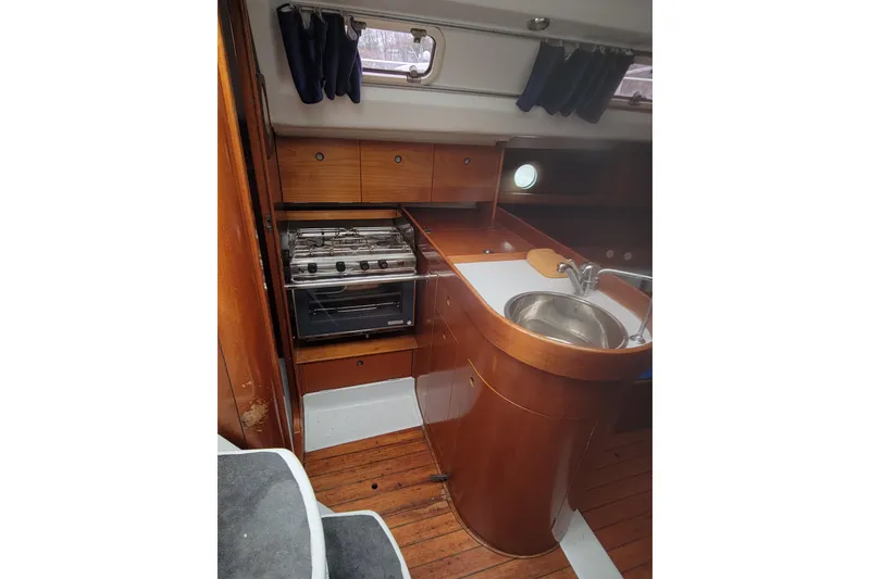 Slide: The Image of Interior of 1994 Beneteau Oceanis 300 sailboat, featuring a compact kitchen with stove and sink. - 6