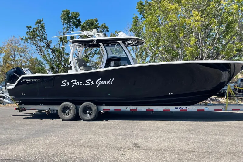 The Image of 2023 Sportsman Open 322 Center Console boat on trailer, black with "So Far, So Good!" text. - 1
