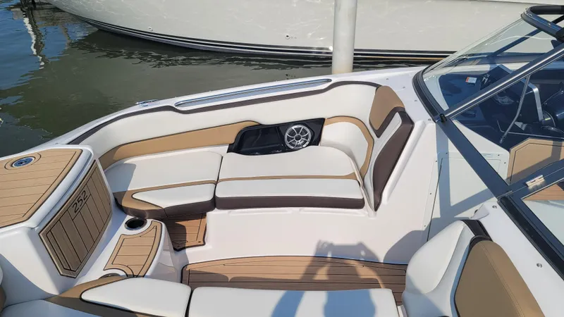 Slide: The Image of 2021 Yamaha Boats 252SD interior with beige seating and speaker, docked by water. - 11