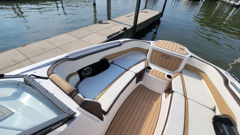 Slide: The Image of 2021 Yamaha Boats 252SD interior with sleek seating and wood accents at a dock. - 13