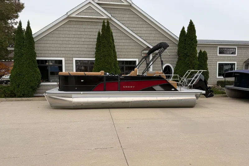 The Image of 2025 Crest Classic 220 pontoon boat parked in front of a building with trees. - 1