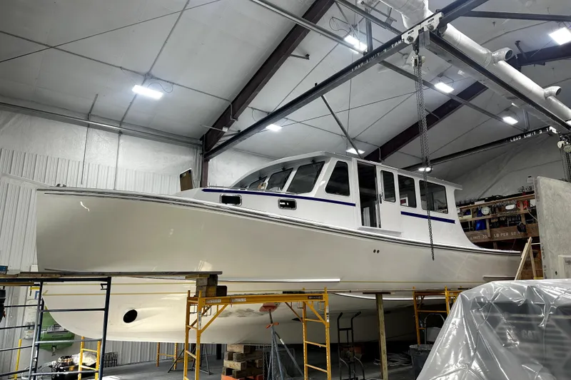 Slide: The Image of 2025 Calvin Beal Sedan boat in a workshop, elevated on scaffolding. - 0