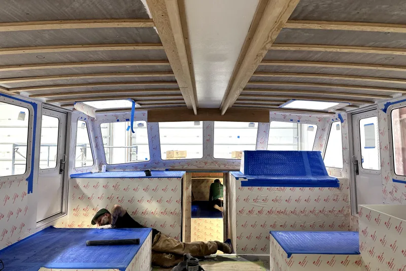 Slide: The Image of Interior of a 2025 Calvin Beal Sedan boat under construction, featuring wood beams and blue protective coverings. - 28