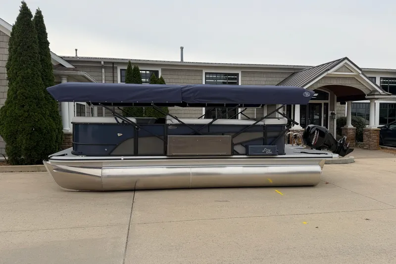 Slide: The Image of 2026 Crest Conquest 210 L pontoon boat with canopy, parked outside a building. - 2