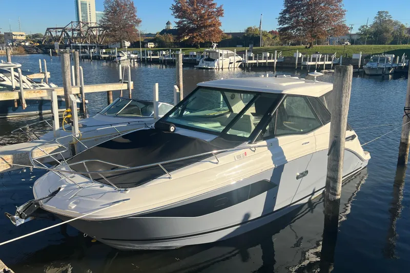 The Image of 2025 Sea Ray Sundancer 320 Coupe docked at marina, surrounded by boats and autumn trees. - 0