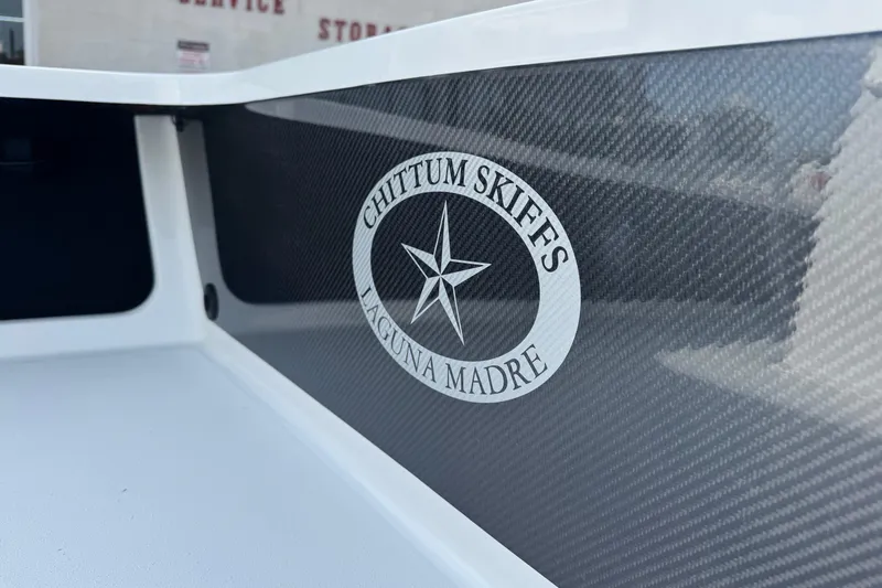 Slide: The Image of 2026 Chittum Skiffs 18 Laguna Madre boat with logo detail on carbon fiber surface. - 7