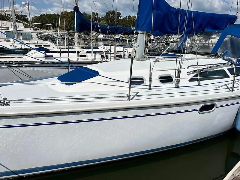 Slide: The Image of 2000 Catalina 320 sailboat docked, featuring sleek white hull and blue sail cover. - 6