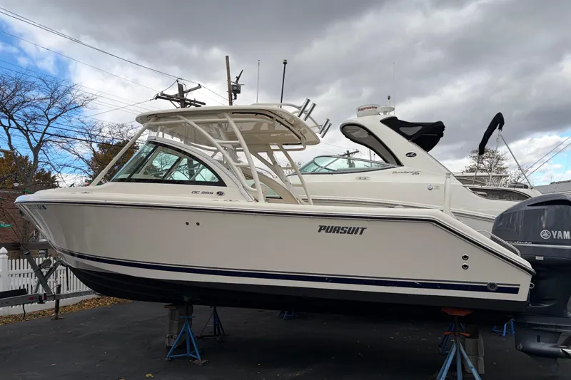 The Image of 2012 Pursuit DC 265 Dual Console boat on stands, overcast sky background. - 0