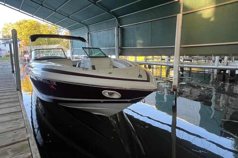 The Image of 1995 Cobalt 252 boat docked under a covered marina, reflecting on calm water. - 1