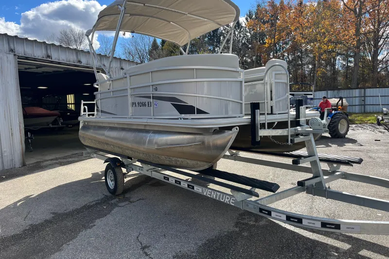 Slide: The Image of 2024 Starcraft LX 16 R pontoon boat on trailer, parked outside a garage. - 7