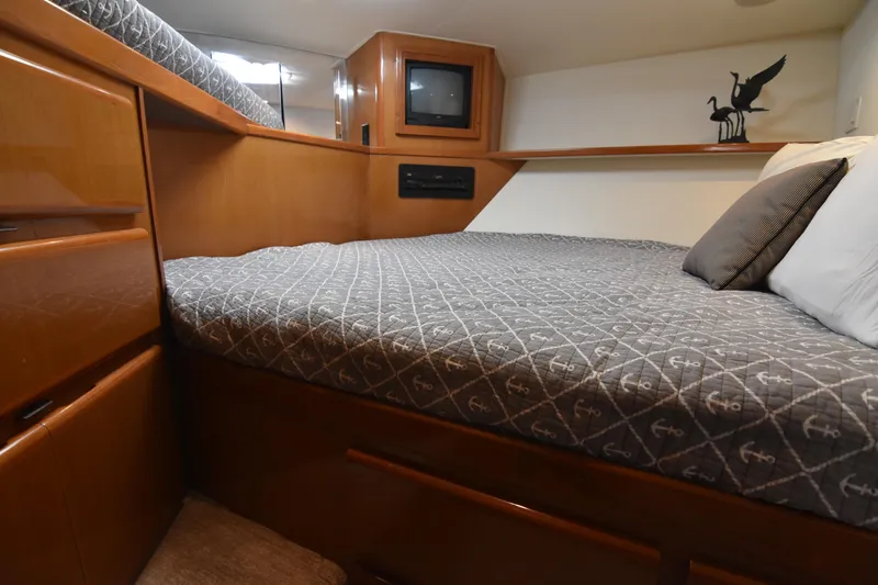 Slide: The Image of 1999 Viking 58 Convertible yacht bedroom with anchor-patterned bedding and wooden cabinetry. - 25