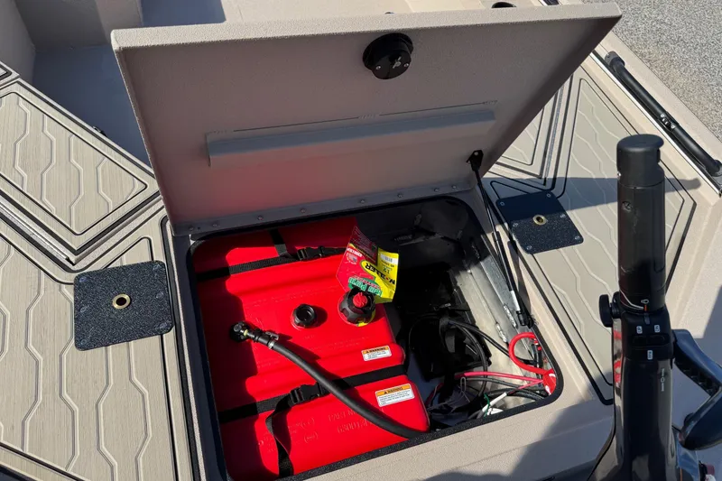 Slide: The Image of Open storage compartment in 2026 Avid 18 Commander boat, revealing red fuel tank and wiring. - 18