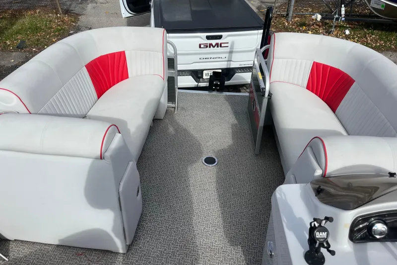 Slide: The Image of 2020 Apex Avanti 820 pontoon boat interior with red and white seating, parked near a GMC Denali. - 2