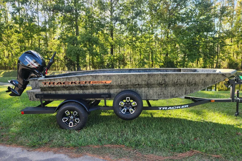 The Image of 2026 Tracker Grizzly 1756 T Marsh boat on trailer, parked on grass with forest background. - 0