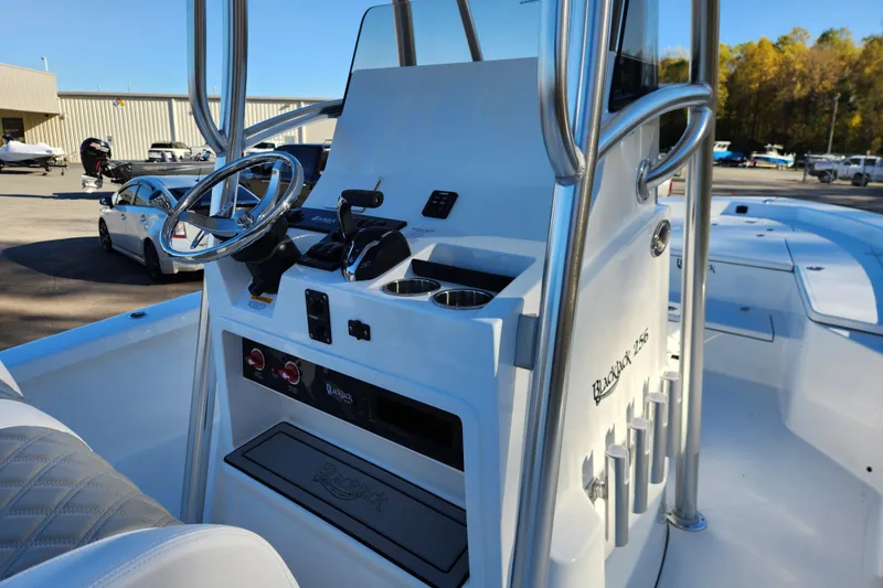 Slide: The Image of 2026 BlackJack 256 Bay boat console with steering wheel and controls in a marina setting. - 12