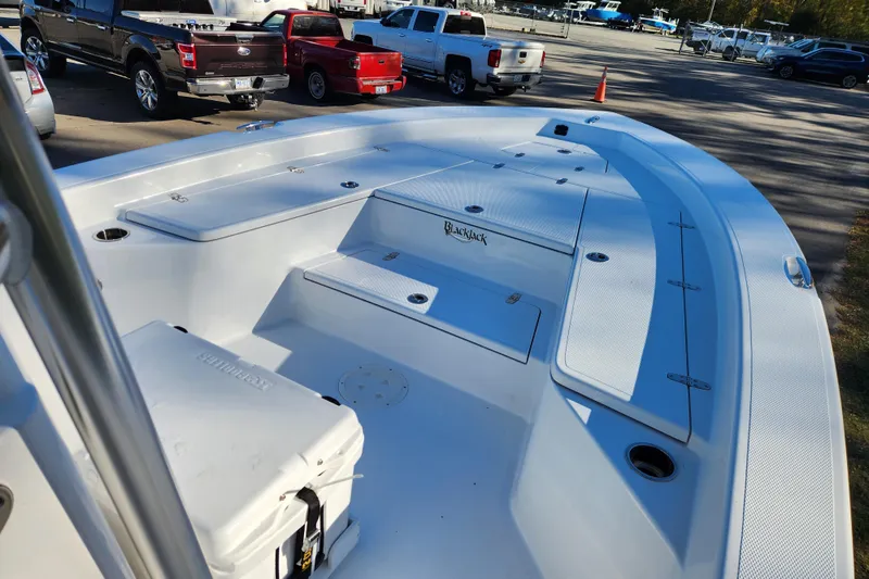 Slide: The Image of 2026 BlackJack 256 Bay boat interior with storage compartments and cooler, parked near trucks. - 8