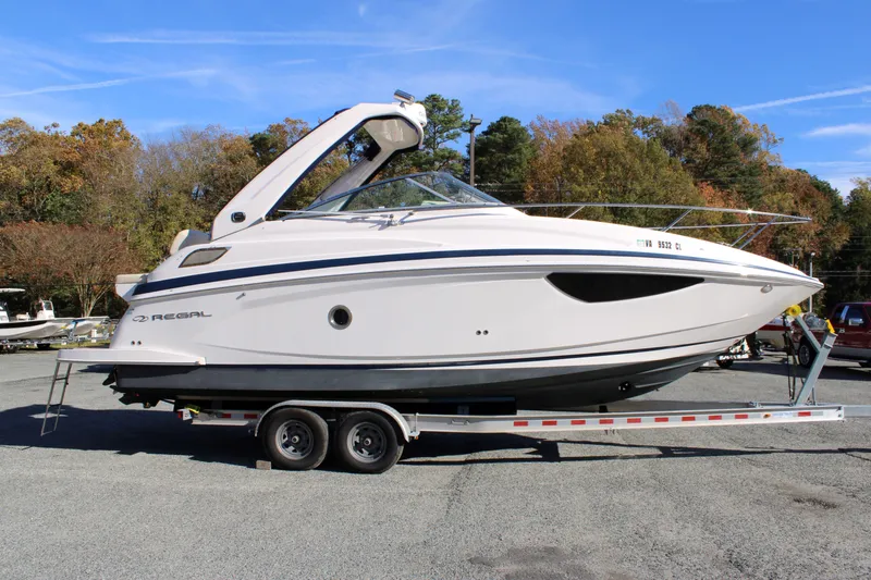 Slide: The Image of 2019 Regal 28 Express boat on trailer, parked outdoors, surrounded by trees. - 4