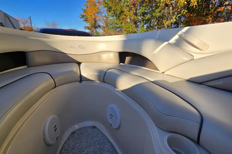 Slide: The Image of 2002 Sea Ray 220 Bow Rider interior with beige seating and speakers, under clear blue sky. - 20
