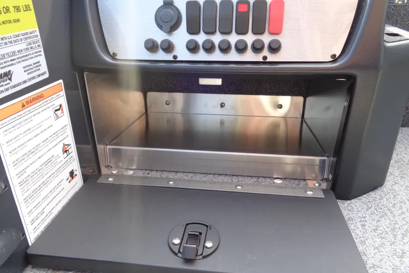 Slide: The Image of 2026 Lund 1650 Angler Tiller control panel with storage compartment and warning labels. - 13