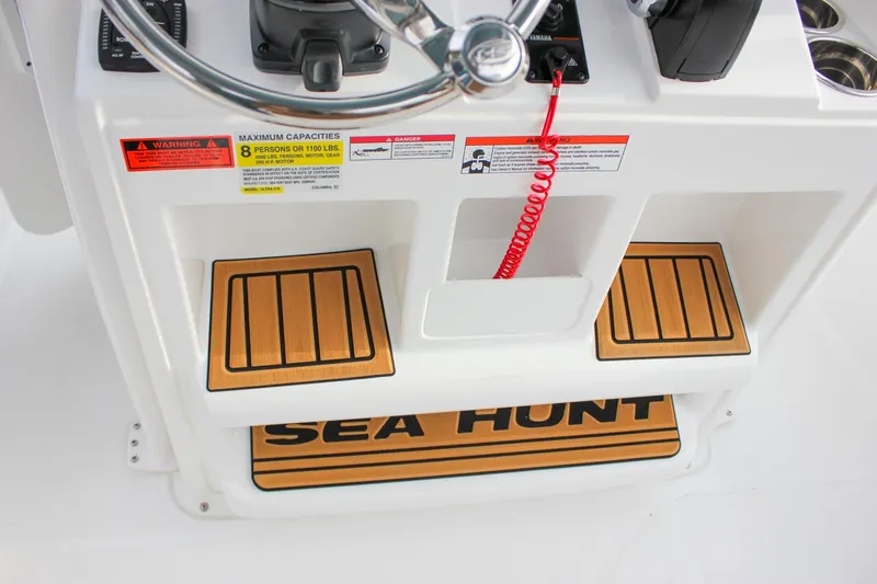 Slide: The Image of 2026 Sea Hunt Ultra 219 boat console with steering wheel and capacity warning labels. - 17