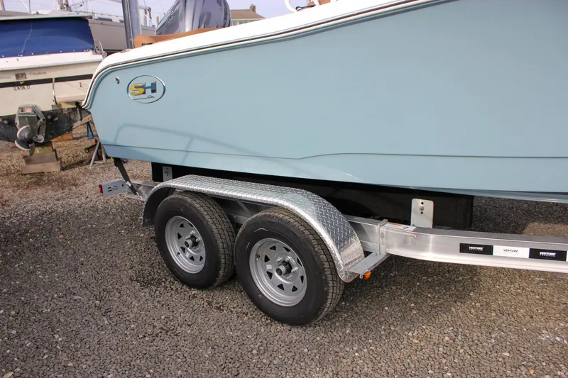 Slide: The Image of 2026 Sea Hunt Ultra 219 boat on a dual-axle trailer, parked on gravel. - 49