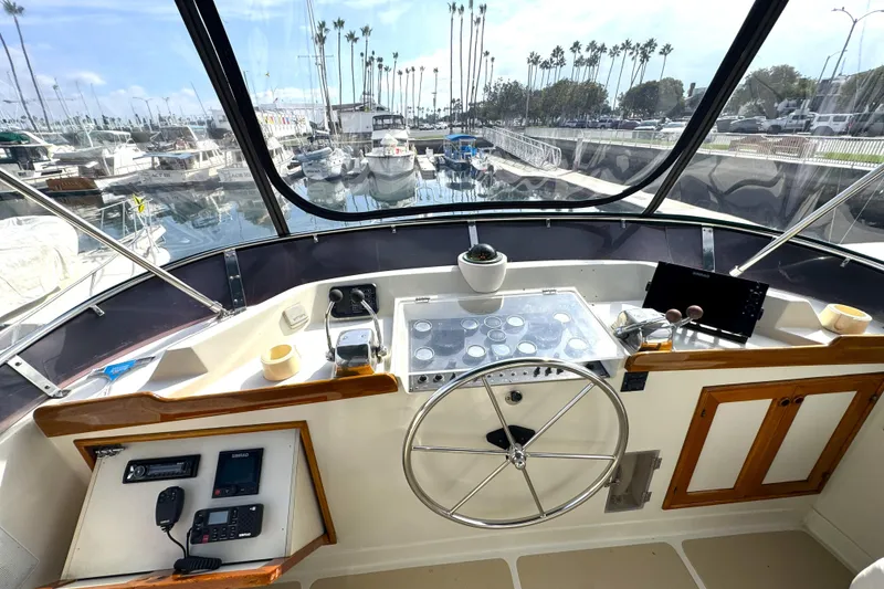 Slide: The Image of Helm of 1988 Offshore Yachts 48 Sedan with marina view, featuring steering wheel and controls. - 16