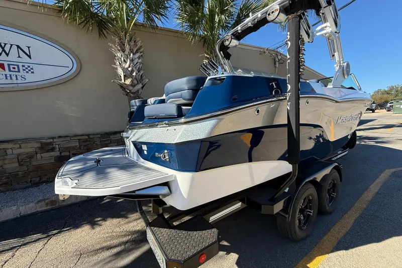 Slide: The Image of 2023 MasterCraft XT23 boat on trailer, parked near palm trees and a building. - 6