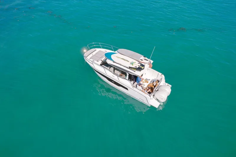 Slide: The Image of 2025 Jeanneau NC895 S2 boat on clear turquoise water, with surfboards on deck. - 10