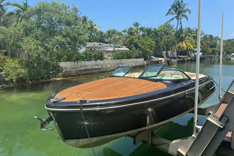 The Image of 2018 Chris-Craft Capri 27 boat on lift, surrounded by lush greenery and calm water. - 0