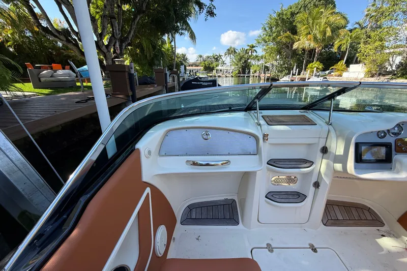 Slide: The Image of 2018 Chris-Craft Capri 27 boat interior with elegant dashboard and seating, docked by lush greenery. - 17