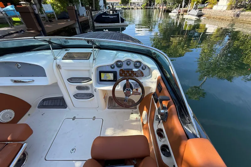 Slide: The Image of 2018 Chris-Craft Capri 27 boat interior with steering wheel and dashboard, docked by a serene waterway. - 21