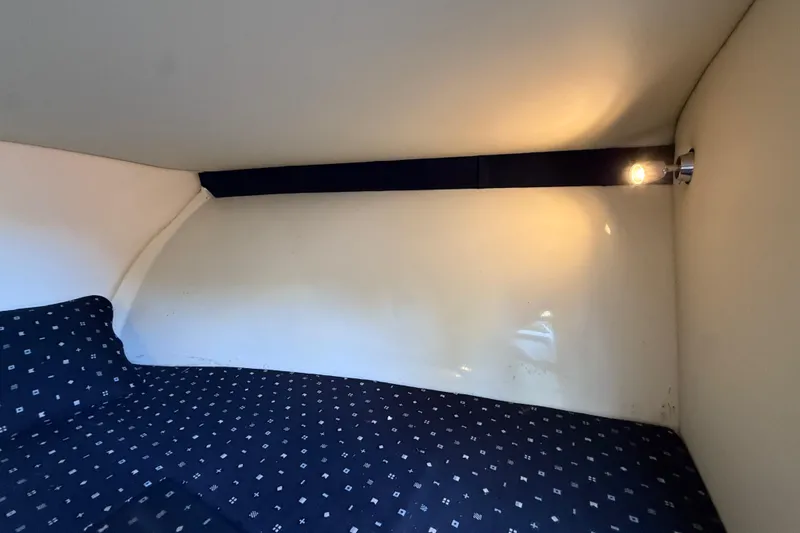 Slide: The Image of 2018 Chris-Craft Capri 27 cabin interior with patterned bedding and wall light. - 38