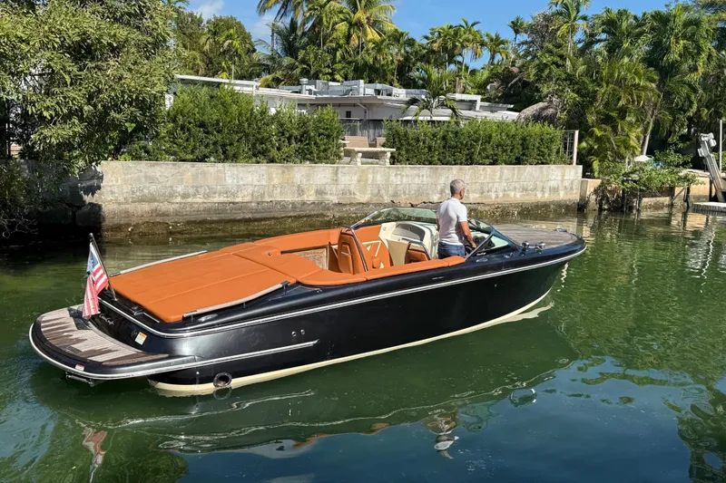 Slide: The Image of 2018 Chris-Craft Capri 27 boat on calm water, surrounded by lush greenery. - 6