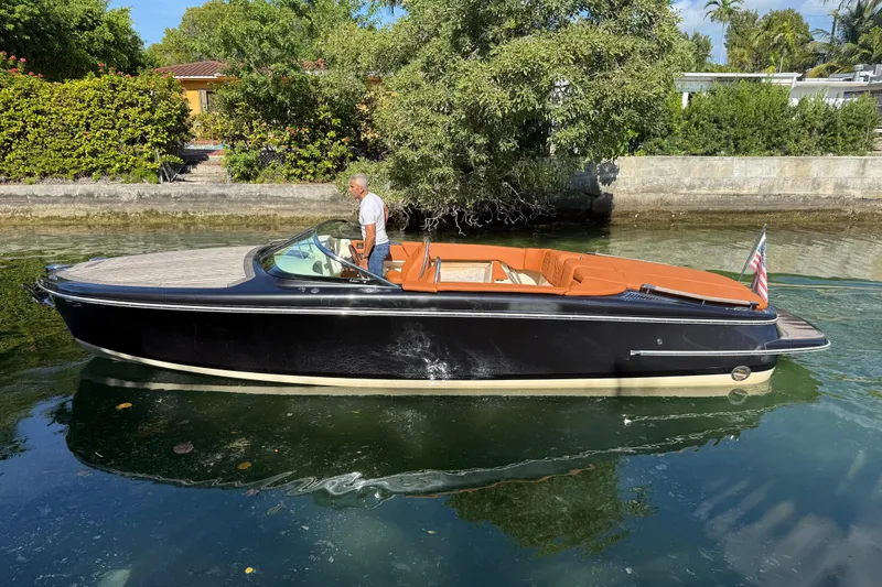 Slide: The Image of 2018 Chris-Craft Capri 27 boat on calm water, featuring sleek black design and tan interior. - 8