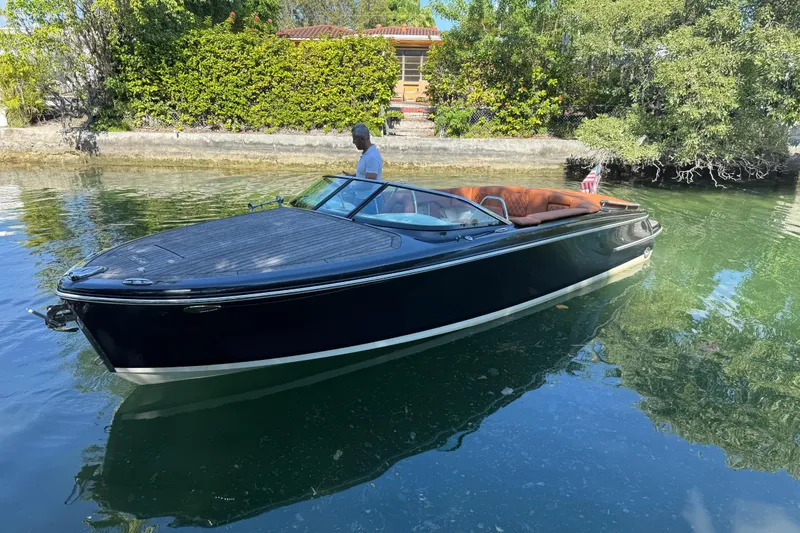 Slide: The Image of 2018 Chris-Craft Capri 27 boat on calm water, surrounded by lush greenery. - 9