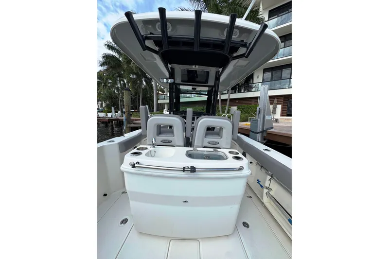 Slide: The Image of 2024 Boston Whaler 280 Outrage boat interior with seating and console, docked near palm trees. - 14