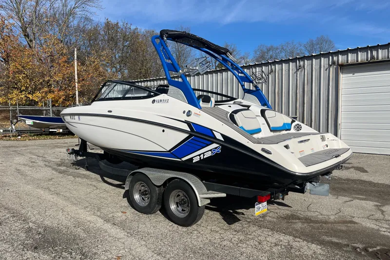 Slide: The Image of 2019 Yamaha Boats 212X on trailer, parked outdoors near a metal building. - 12