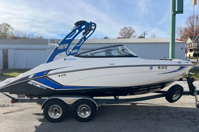 Slide: The Image of 2019 Yamaha Boats 212X on trailer, white and blue design, parked outdoors. - 14