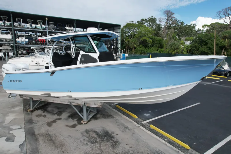 The Image of 2023 Blackfin 332 CC boat in light blue, parked on a stand in a marina. - 0